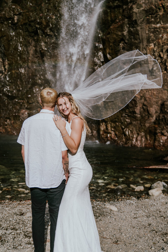 Groom and bride next to waterfall with bride's veil flying in the wind