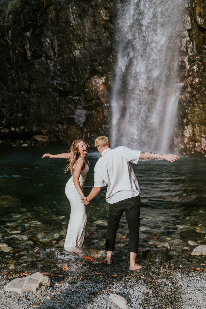 Bride and groom run into waterfall together in their wedding attire
