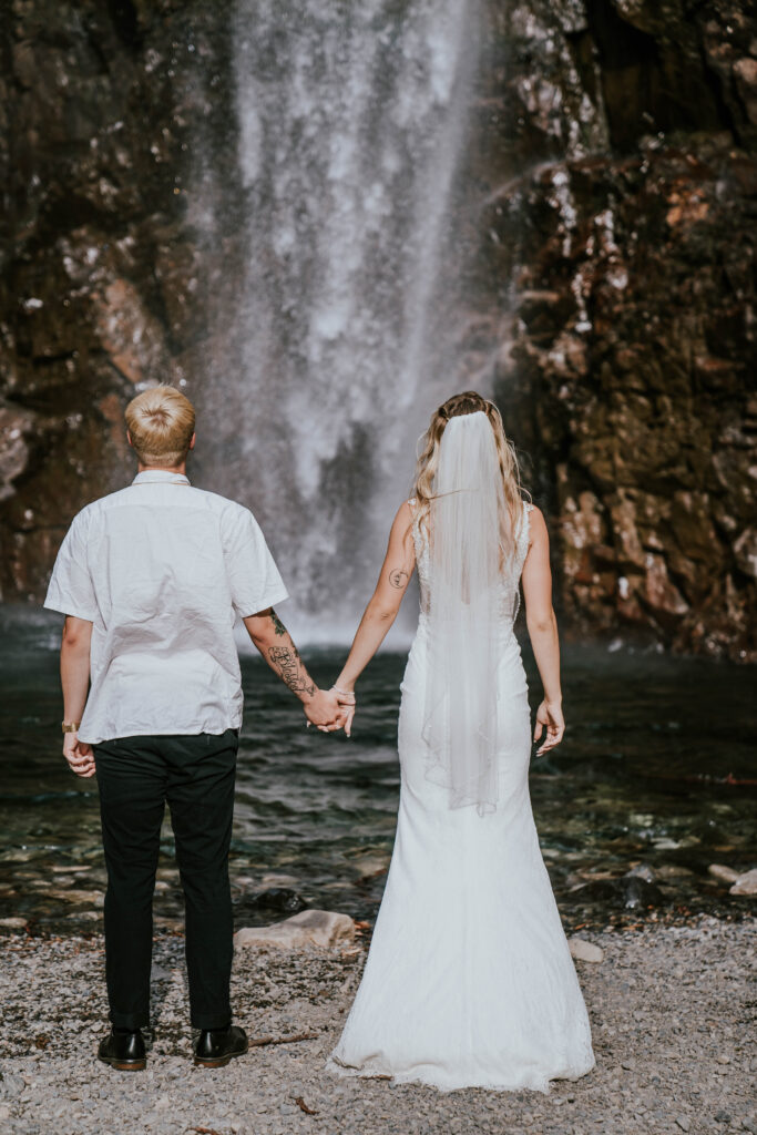 Bride and groom holding hands facing the waterfall
