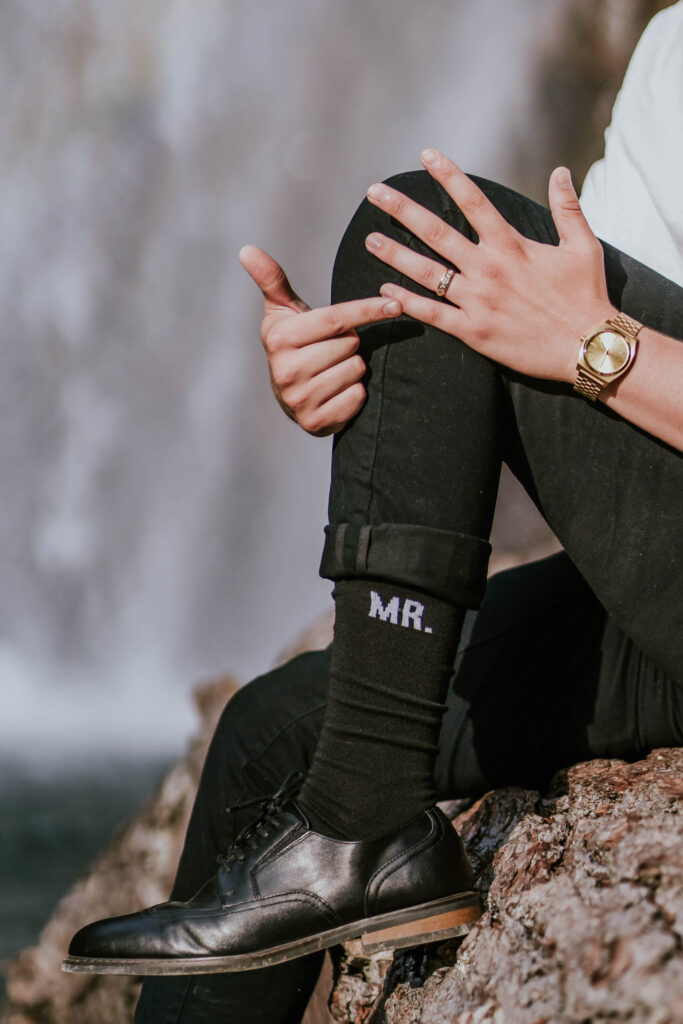 Groom pointing to his ring while wearing socks that say "Mr."
