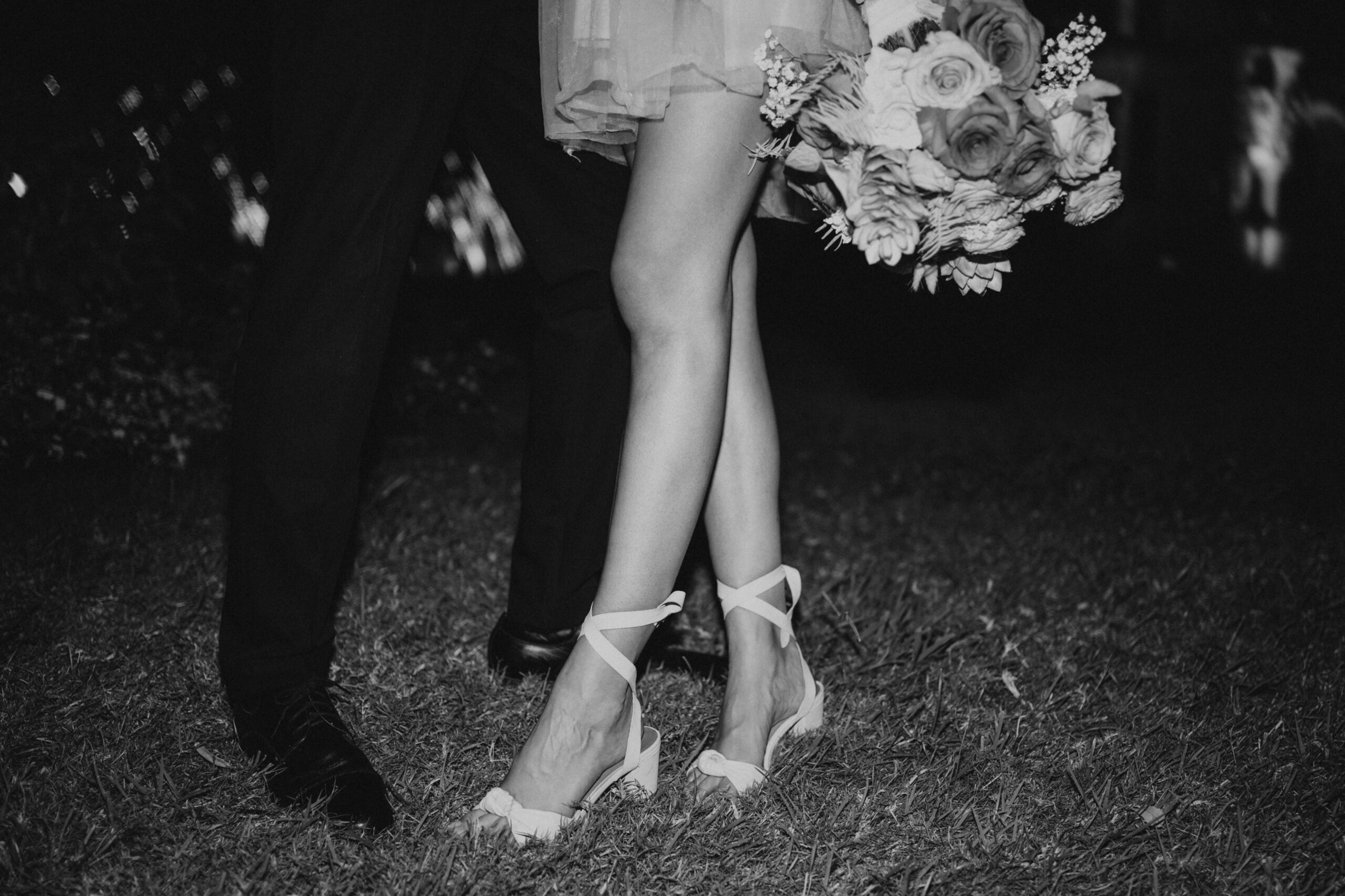Black and white wedding portrait of bride and grooms legs with floral bouquet