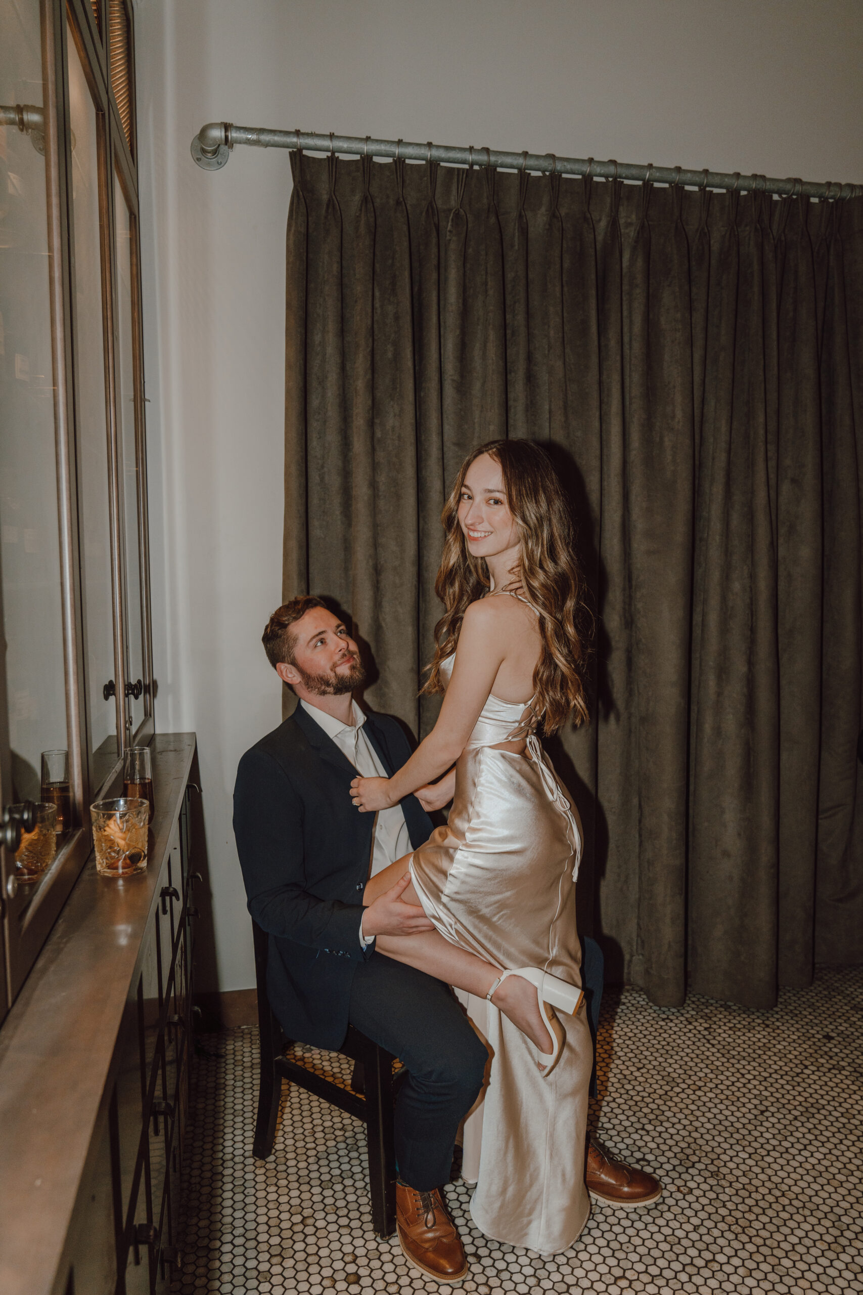 Engagement photos in a bar with drinks, girl in a long satin dress, and male in navy blue suit