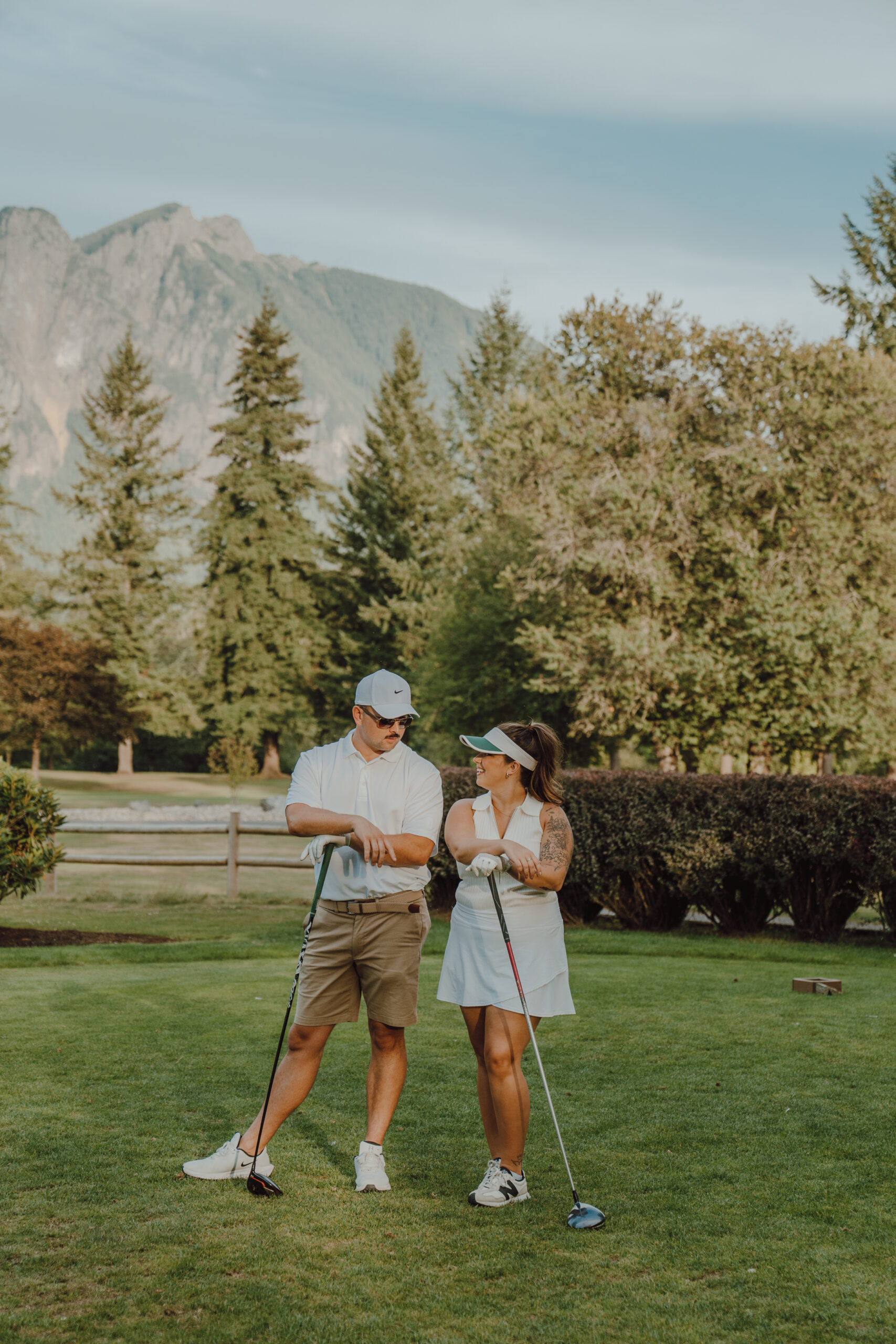 Couple posing on golf course with clubs in front of Mount Is